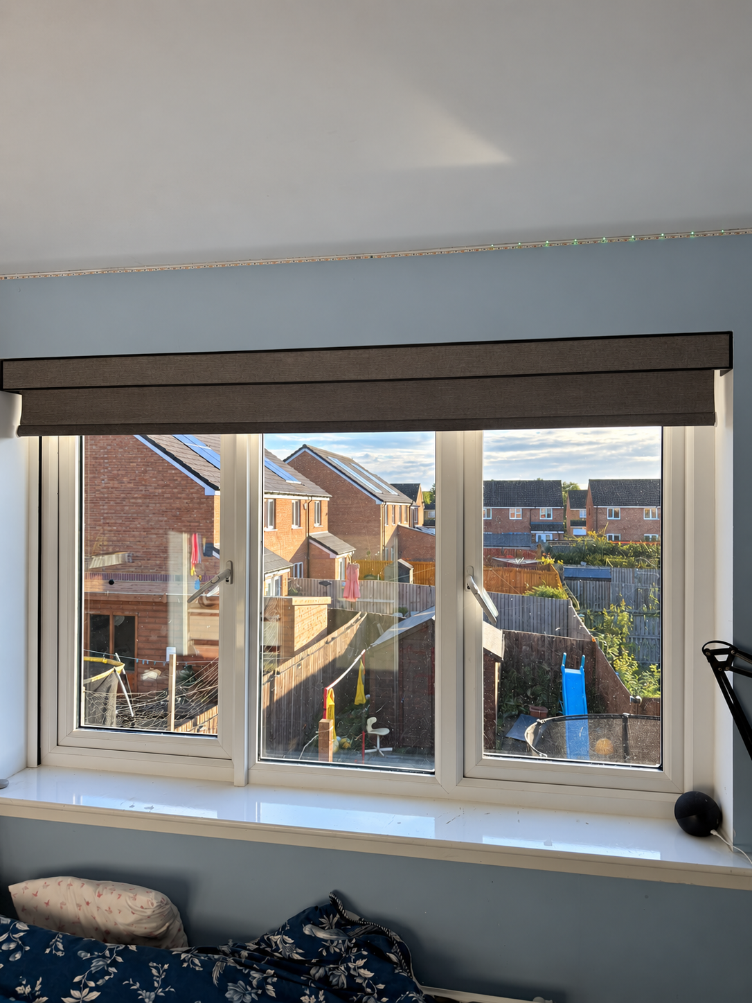 Grey motorised roller blind raised above a bedroom window
