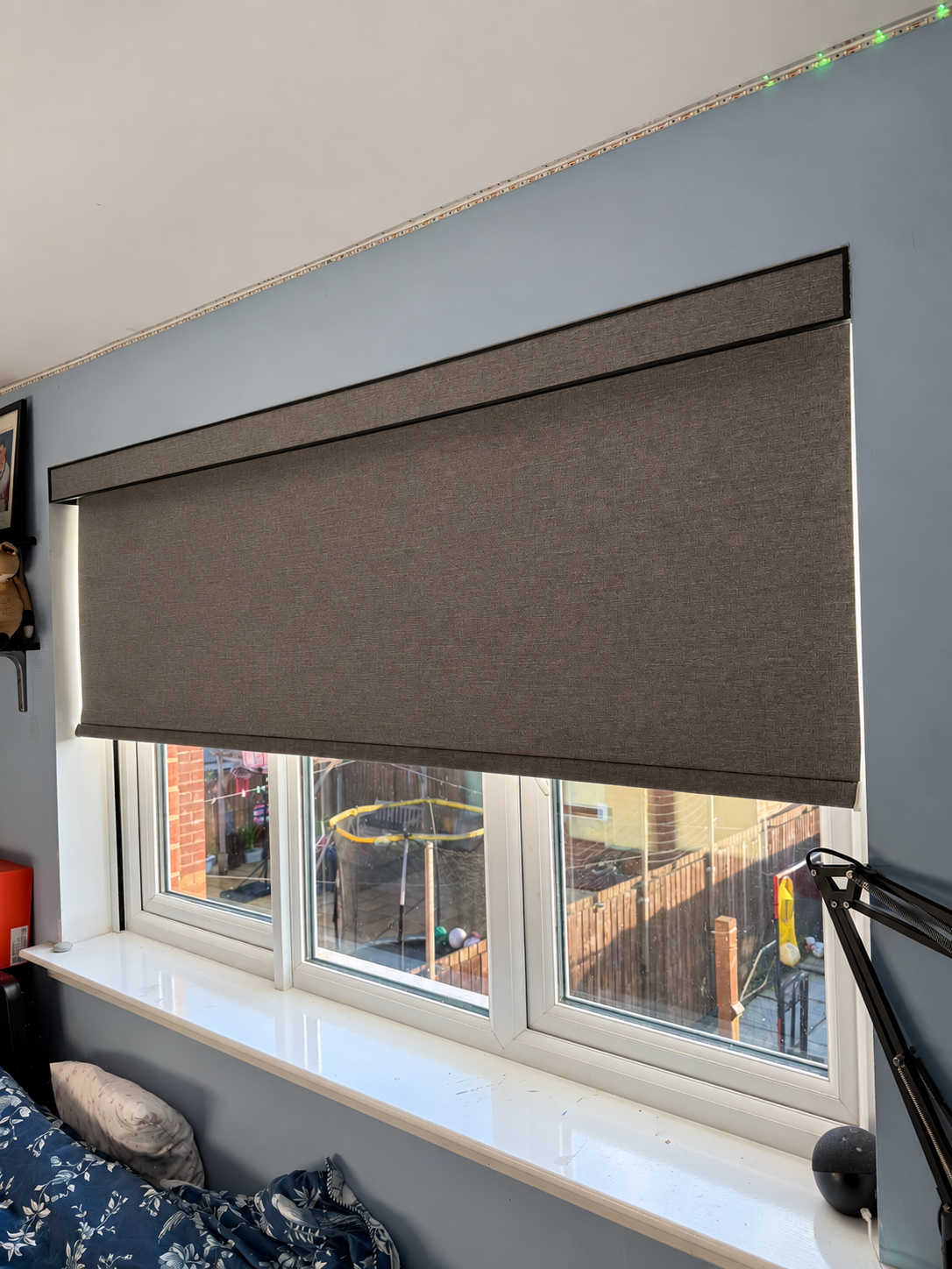 Grey motorised roller blind lowered over a bedroom window