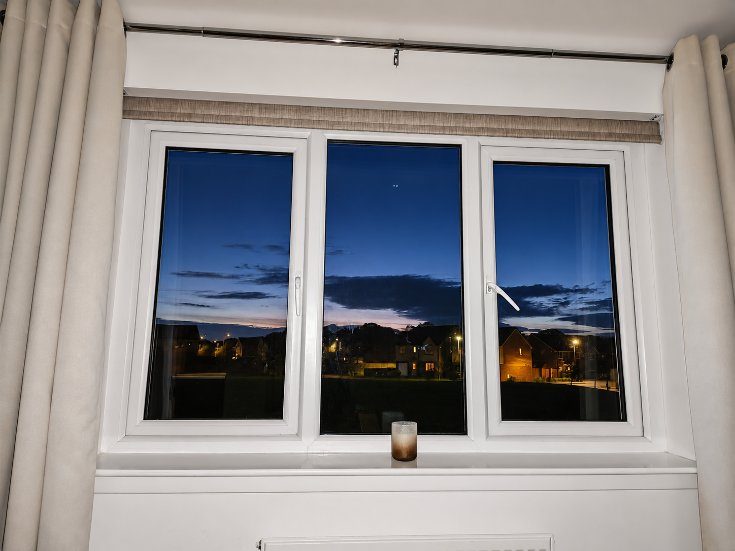 Neutral motorised roller blind installed behind curtains