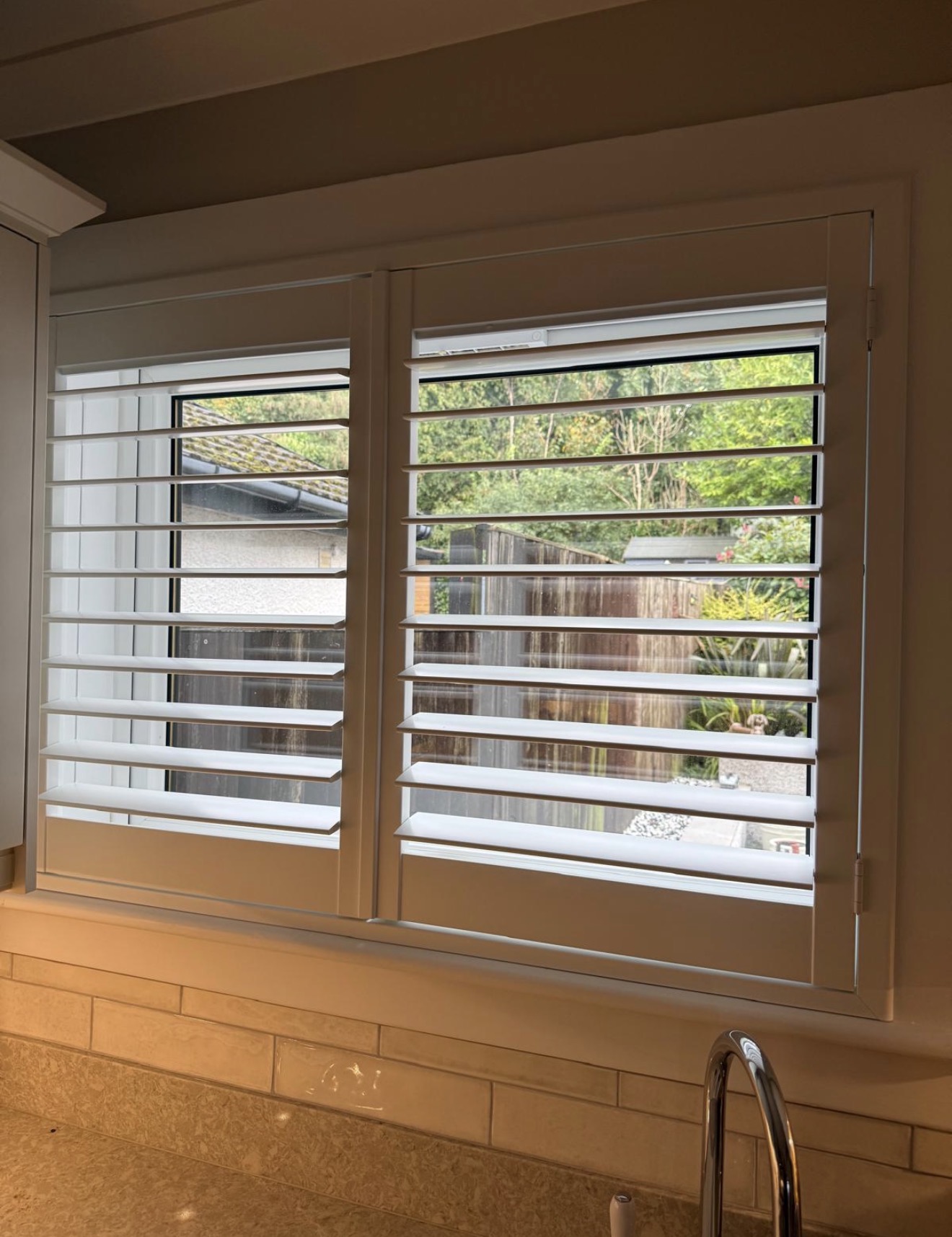 White plantation shutters fitted above a kitchen sink with the louvres open