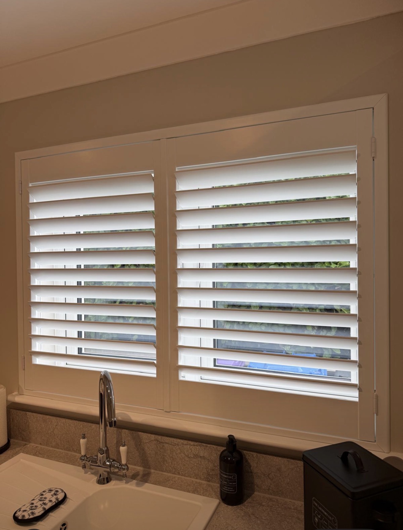 White plantation shutters above a kitchen sink with tilted louvres
