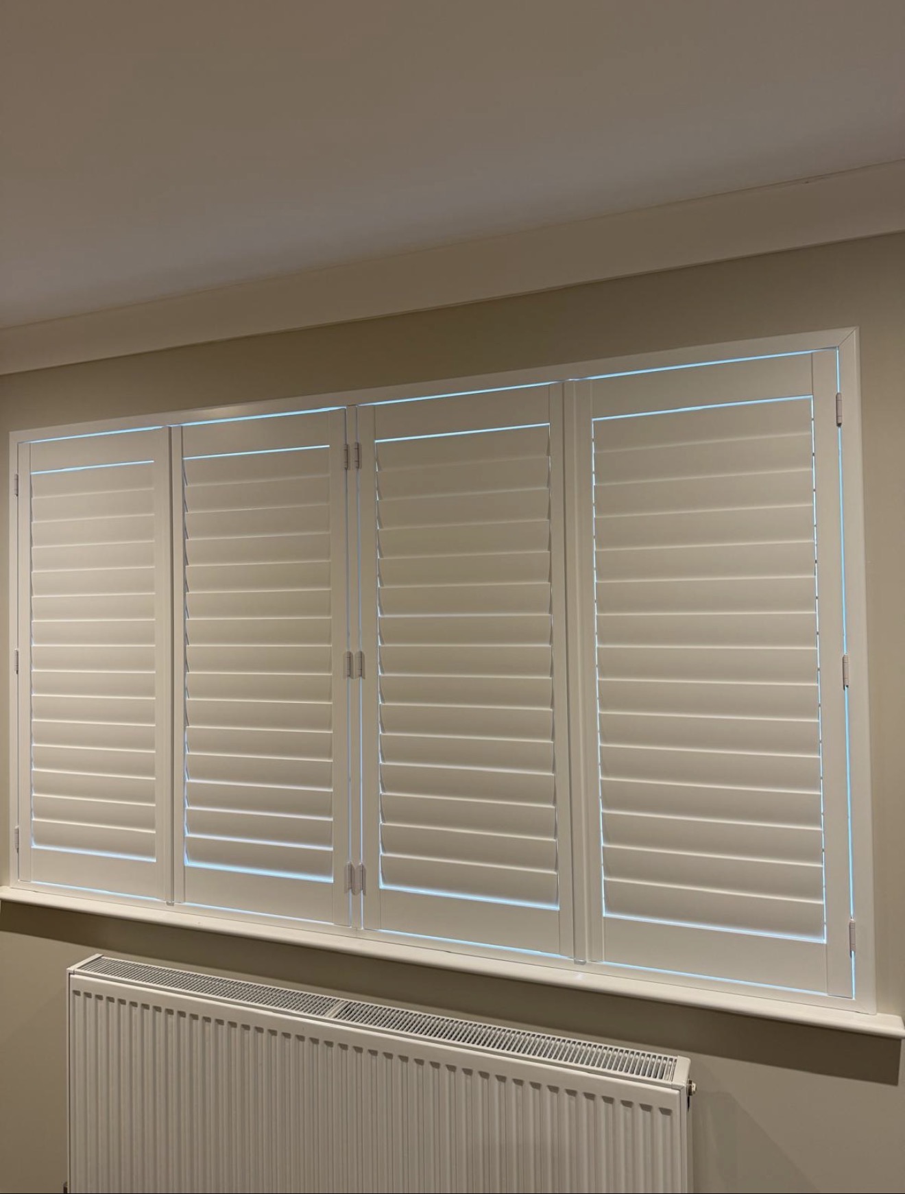 Four-panel white plantation shutters closed across a wide window